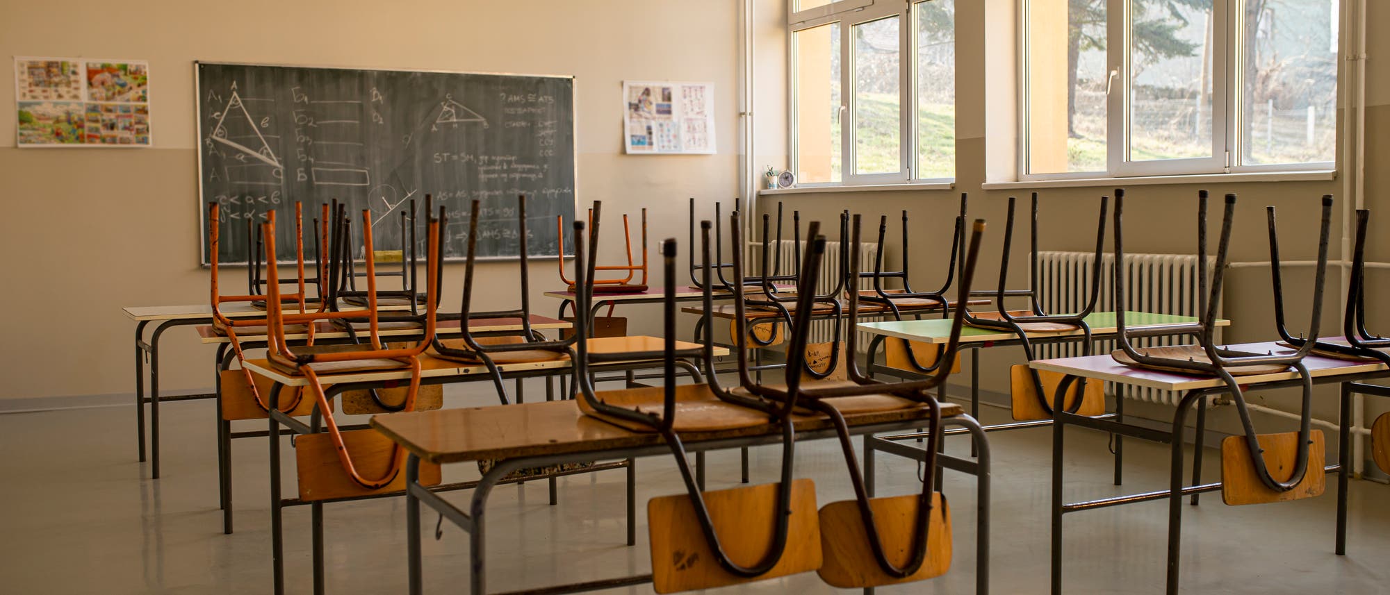 Blick in ein Klassenzimmer mit Kreidetafel und hochgestellten Stühlen