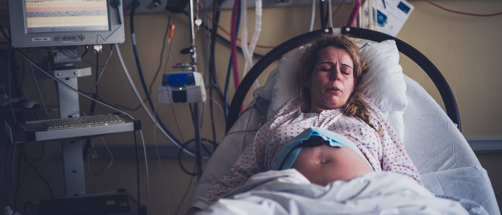 Eine schwangere Frau liegt in einem Krankenhausbett und hat ofensichtlich Wehen.