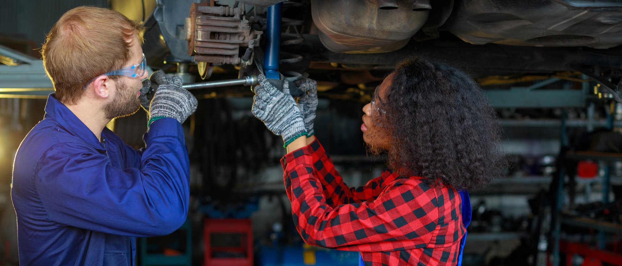 Eine junge Frau und ein junger Mann reparieren ein Auto in einer Werkstatt