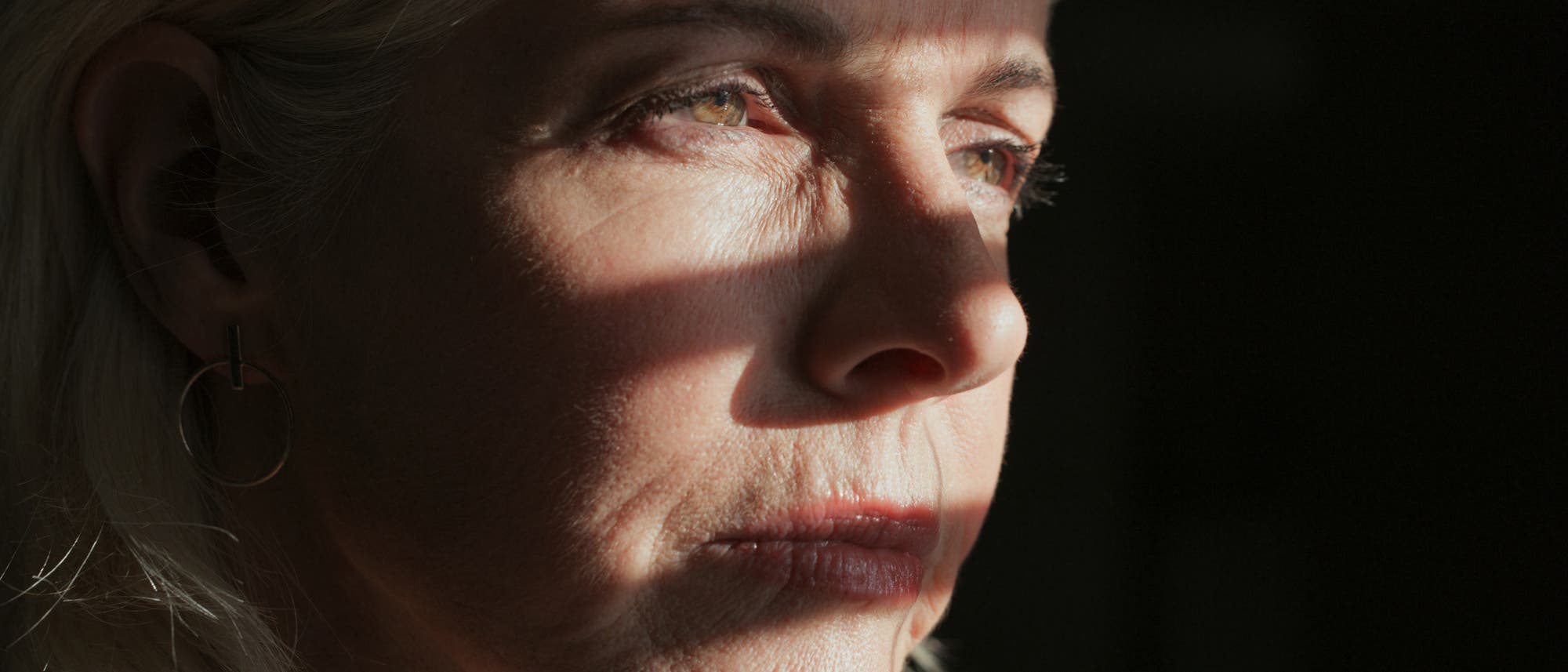 Gesicht einer ernst blickenden Frau in Großaufnahme, teilweise im Schatten, teilweise beleuchtet