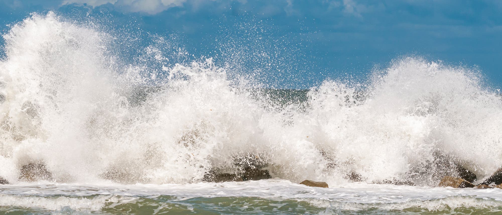 Eine Welle bricht an einem Wellenbrecher und erzeugt eine Gischtwolke.