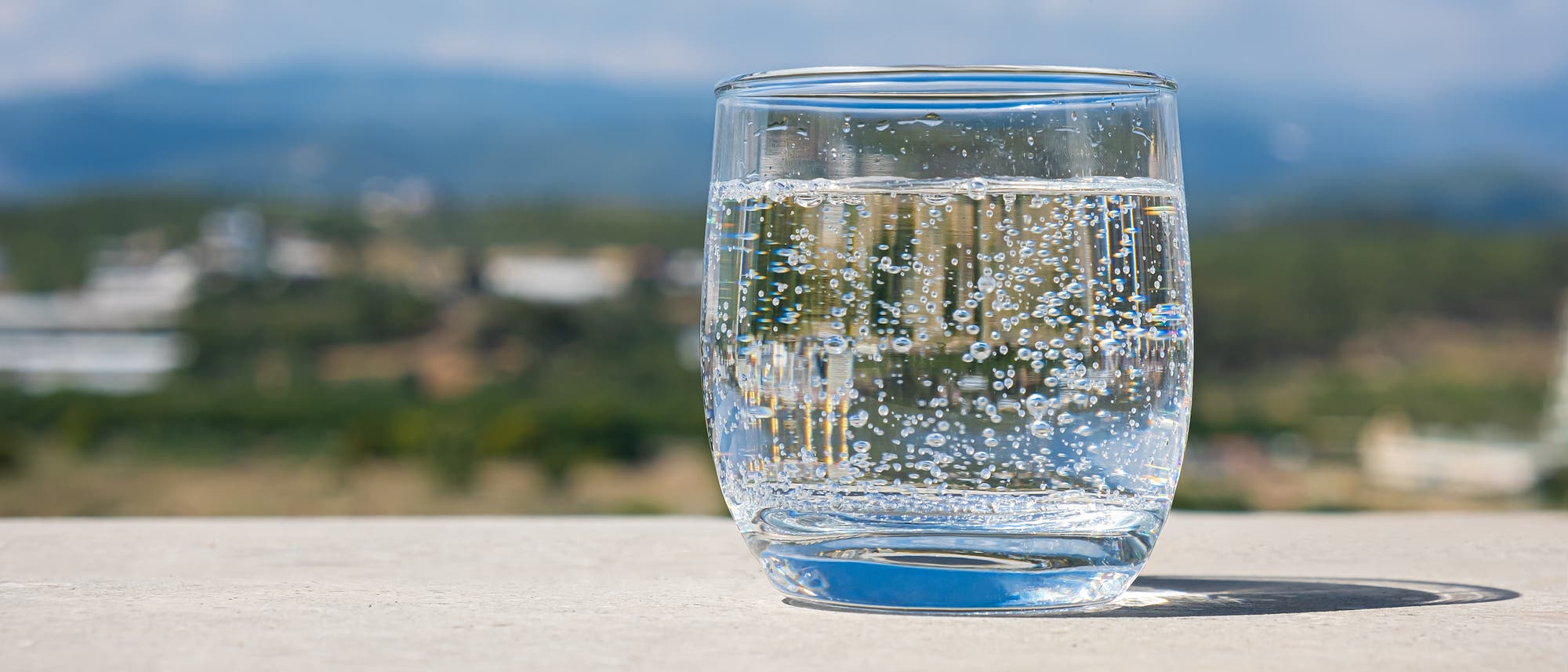 Ein Glas mit Sprudelwasser steht auf einem Mäuerchen