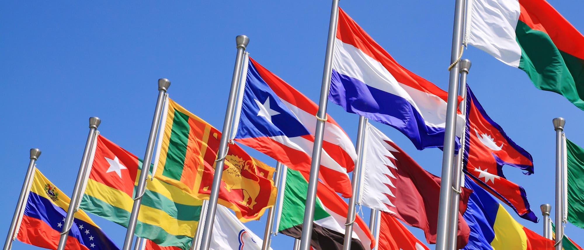 Diverse Nationalflaggen an eng stehenden Fahnenmasten.