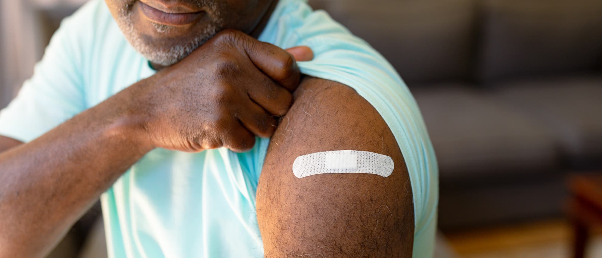Afroamerikanischer, älterer Mann zeigt nach der Impfung seinen Oberarm mit Pflaster