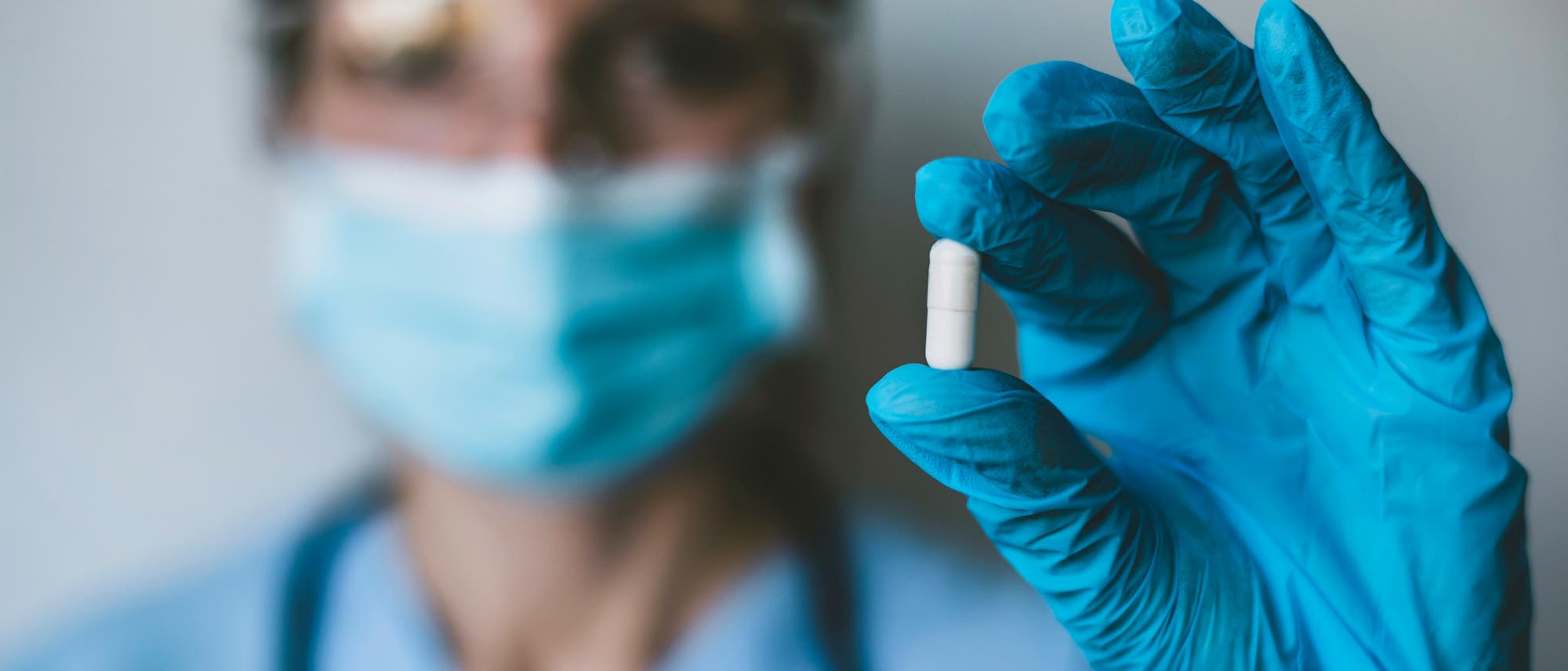 Medizinerin mit Mundschutz hält antivirale Pille in die Kamera