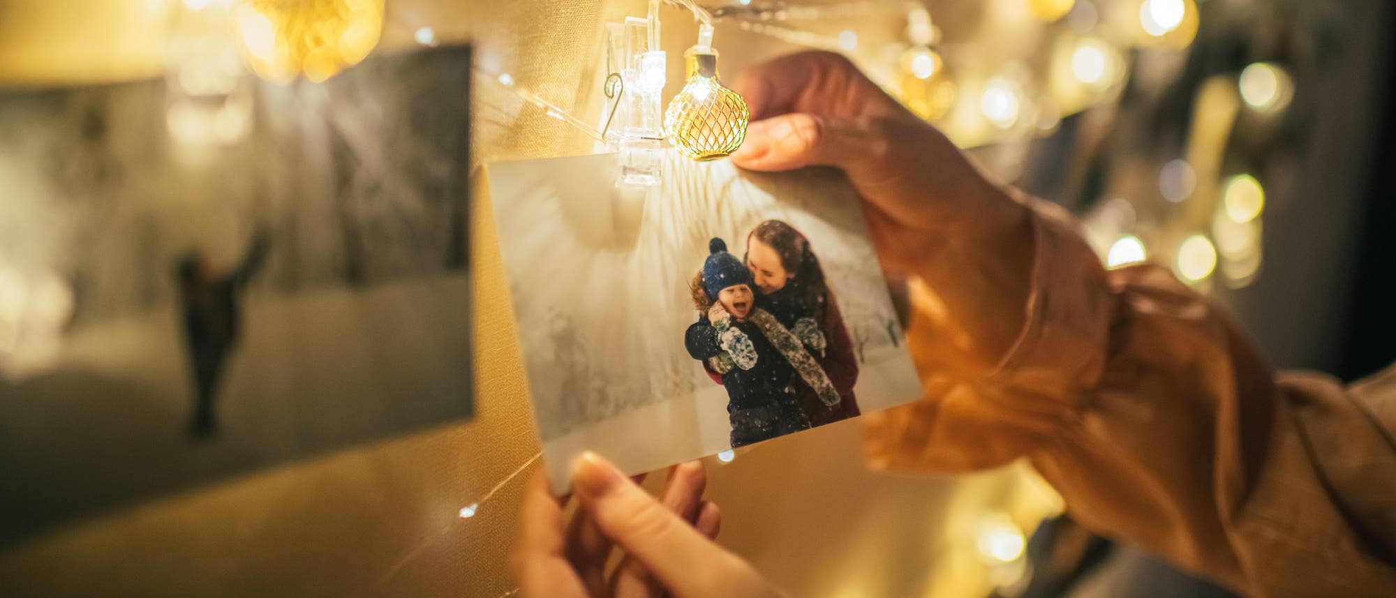 Familienfoto hängt an einer Lichterkette. Zwei Hände greifen danach.