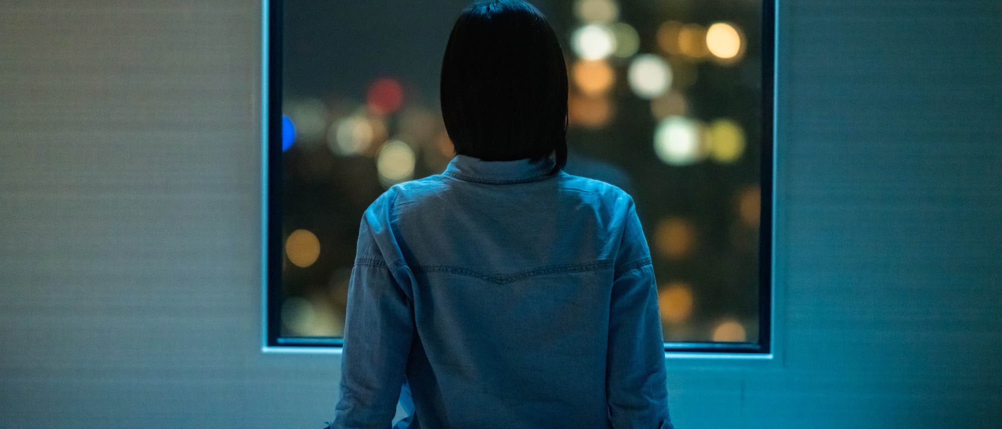 Frau blickt durchs Fenster auf Lichter in der Nacht