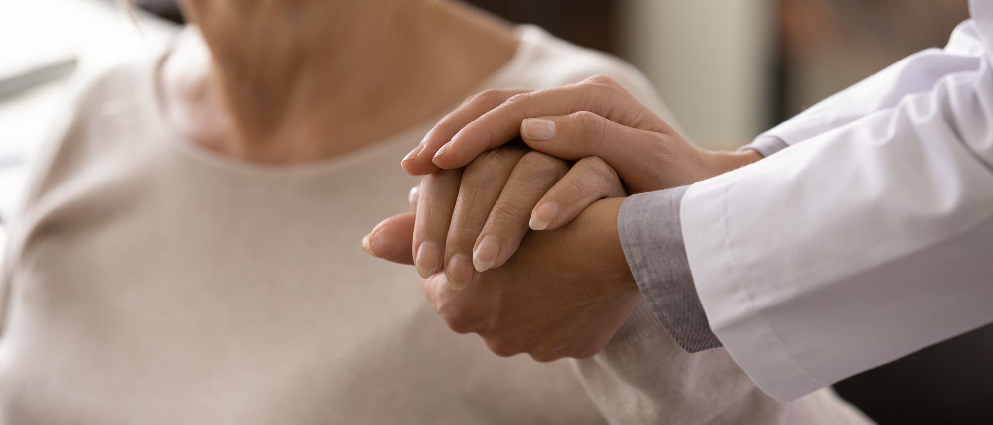 Ein Ärztin stützt mit einer Hand und bedeckt mit ihrer anderen die Hand einer Patientin.