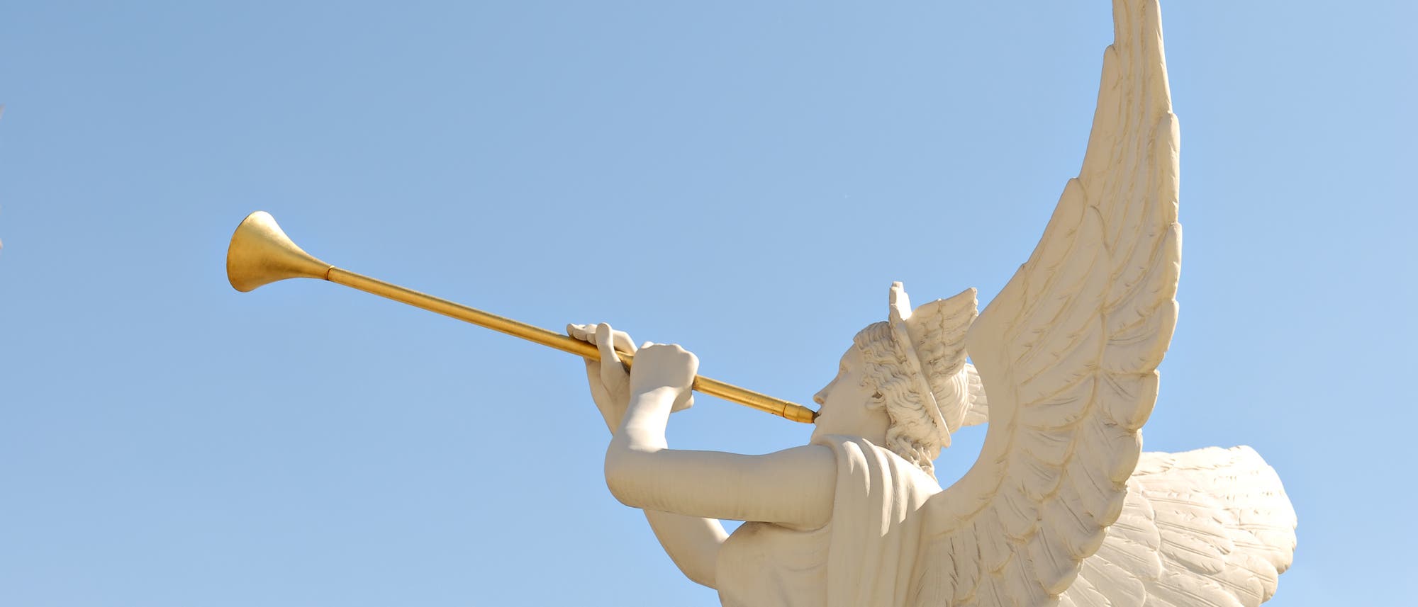 Eine Engelsstatue mit goldener Trompete gegen blauen Himmel fotografiert.
