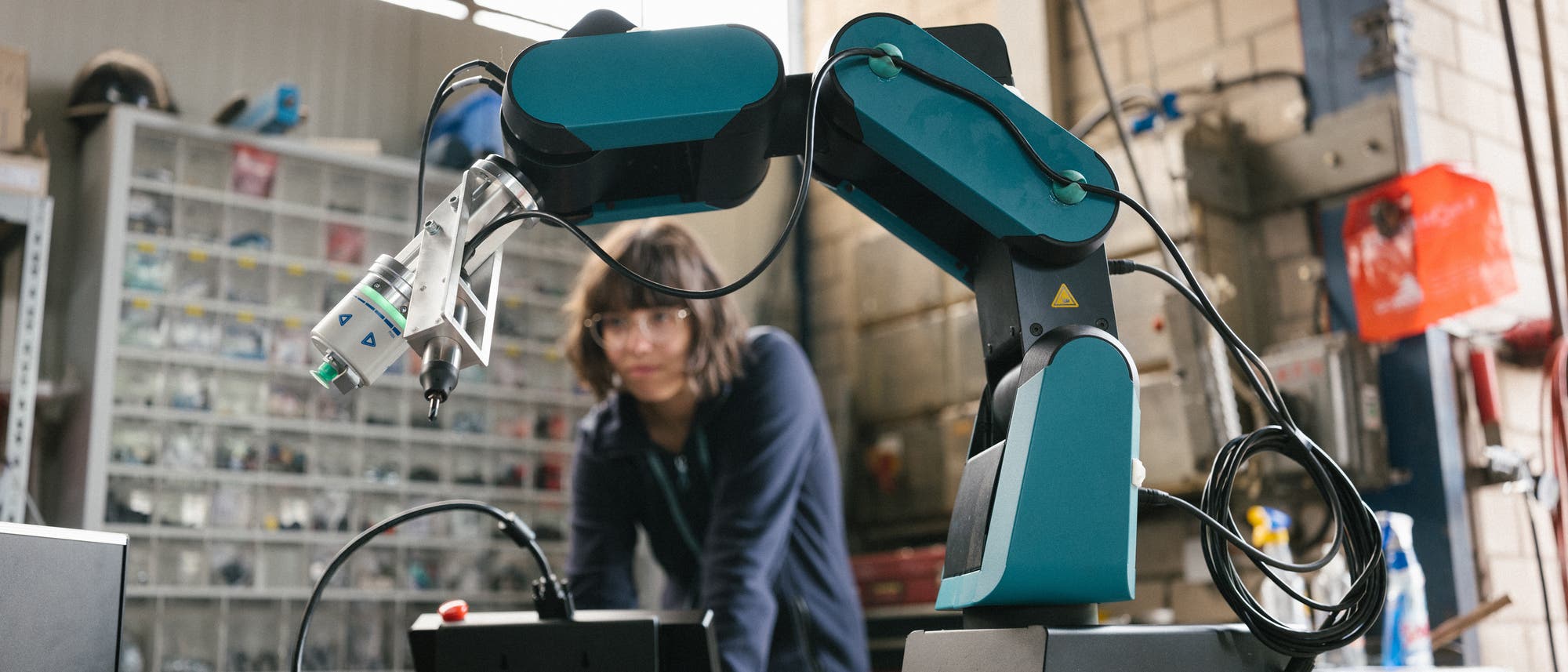 Eine Technikerin hinter einem grünen Roboterarm in einer Werkstatt.