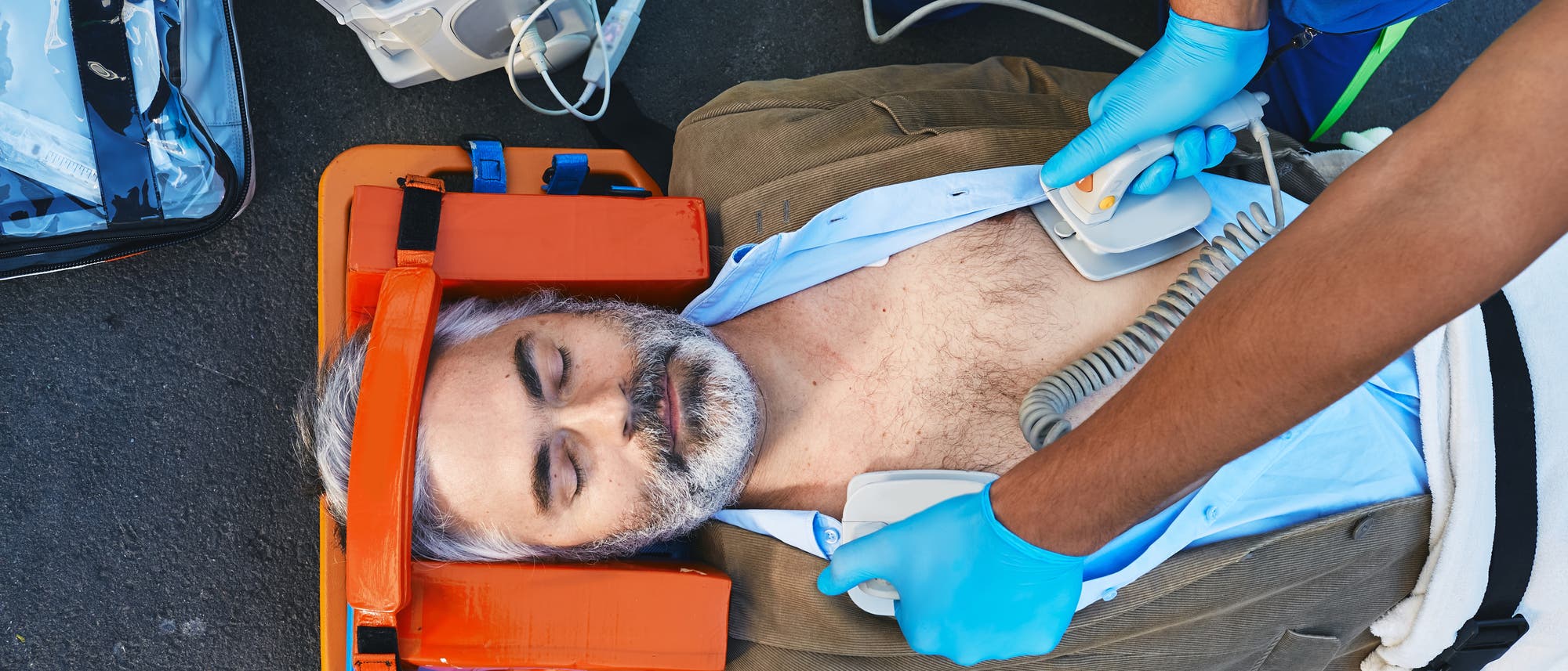 Grauhaariger Mann liegt auf dem Boden und wird mit einem Defibrillator behandelt