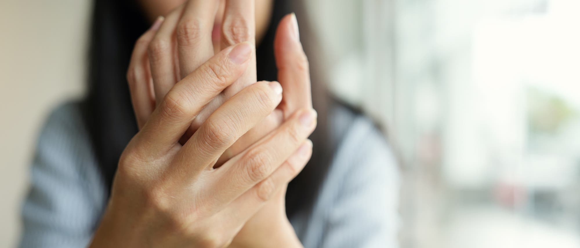 Eine Frau verschränkt ihre Hände in einer schmerzhaft anmutenden Geste