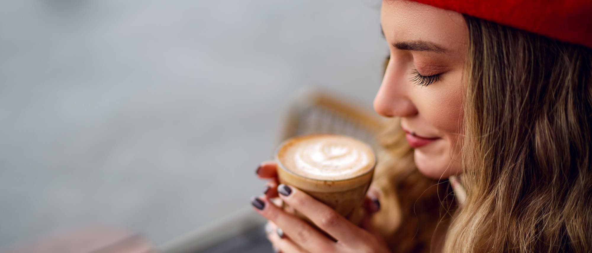 Eine Frau sitz in einem Café und riecht an einer Tasse Kaffee.