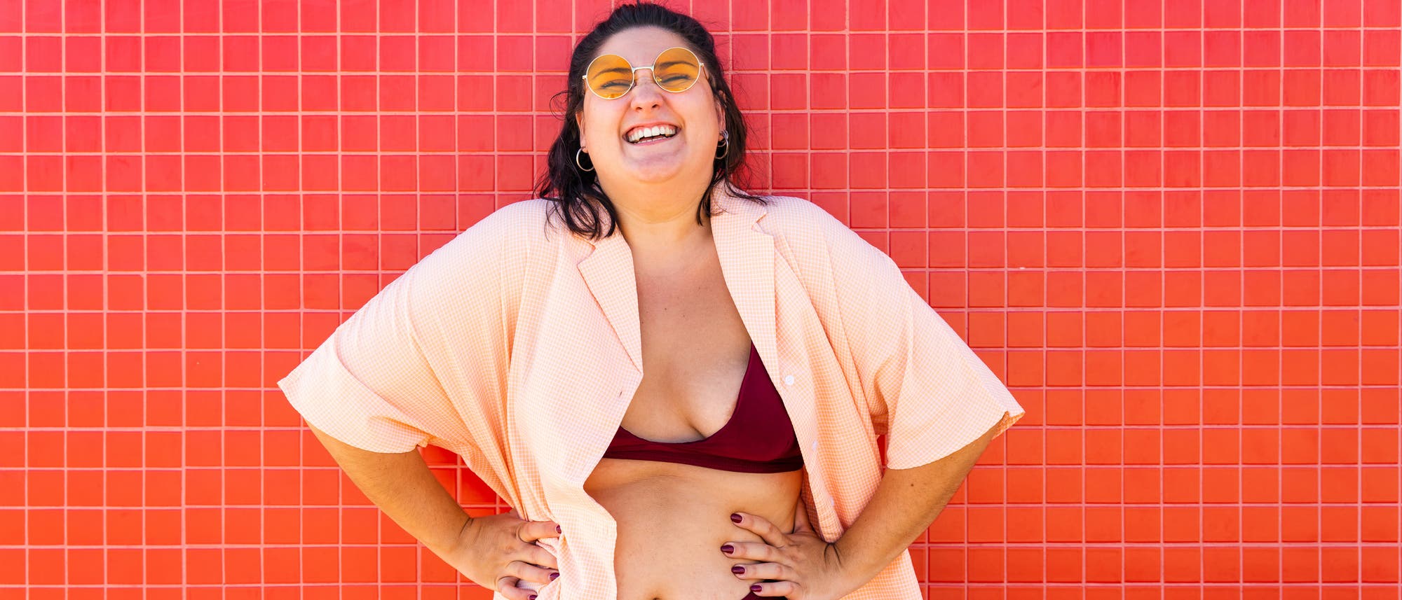 Eine Frau im Bikini steht lachend vor einem roten Hintergrund