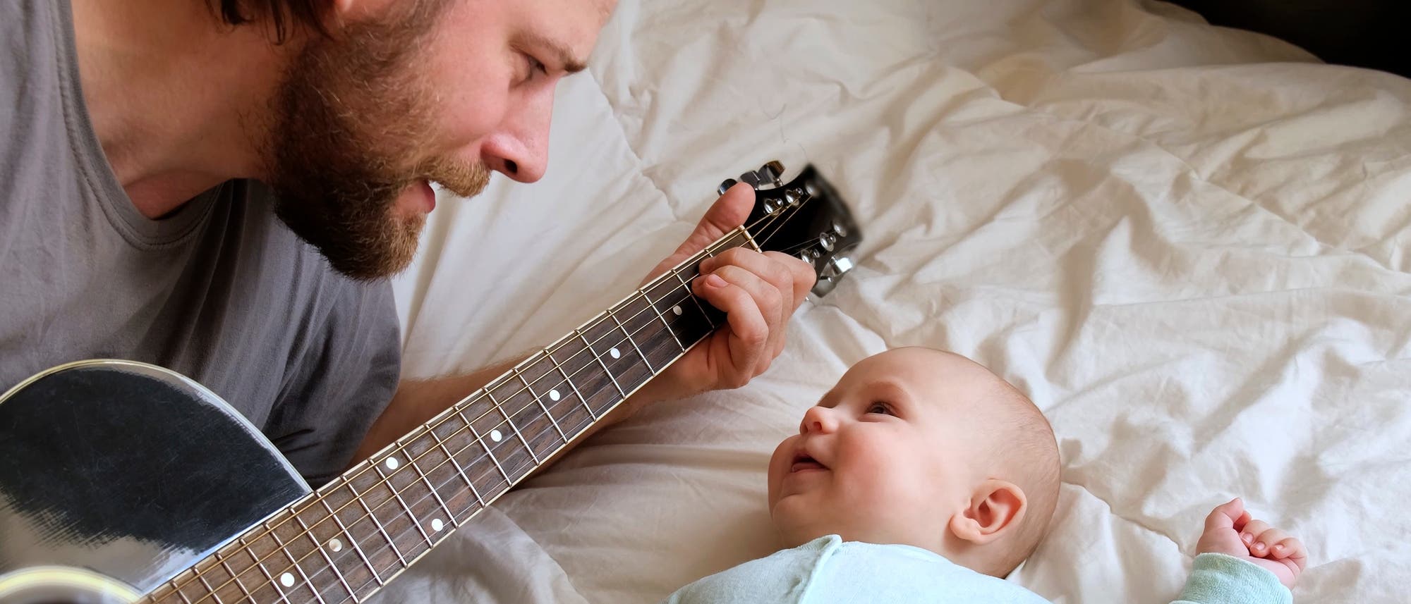 Ein Mann hat spielt ein Lied auf der Gitarre einem Baby vor, das ihn vergnügt anschaut.