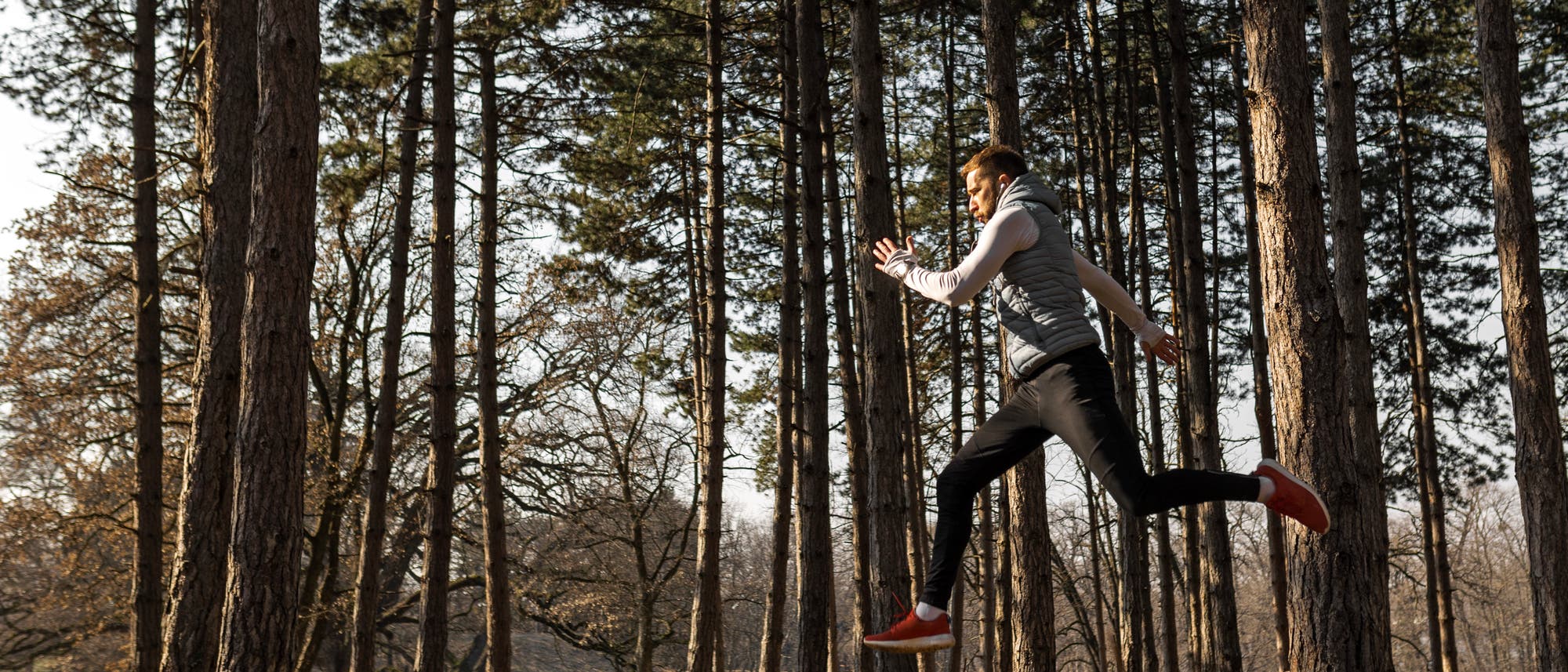 Ein Mann joggt im Wald und federt dabei sehr mit den Füßen ab, so dass er vom Boden abhebt