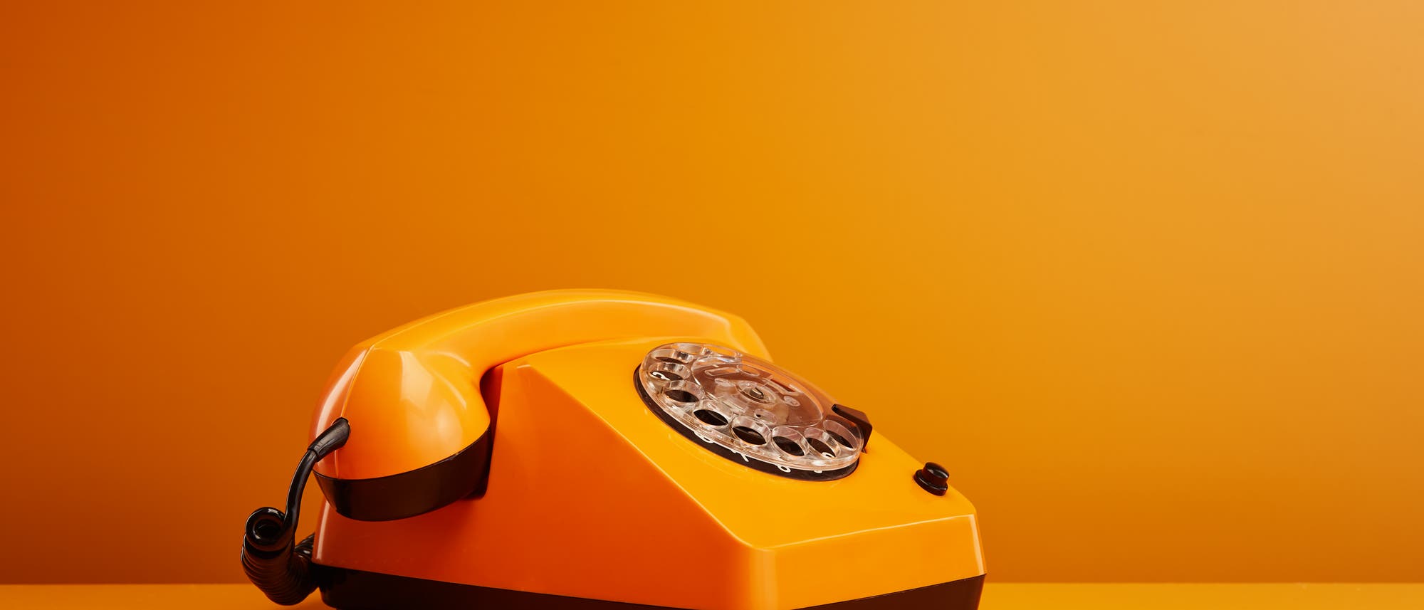 Organgenes Wählscheibentelefon vor orangenem Hintergrund