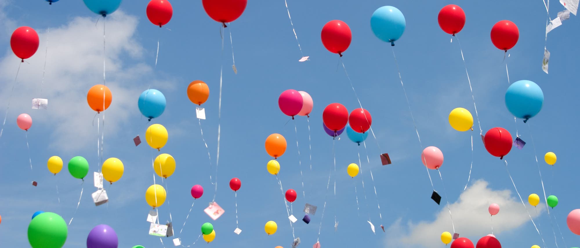 Ballons mit Postkarten dran steigen in den blauen Himmel auf.