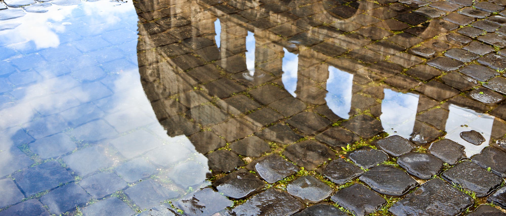 Das Kolosseum spiegelt sich malerisch in einer Wasserpfütze auf Kopfsteinpflaster