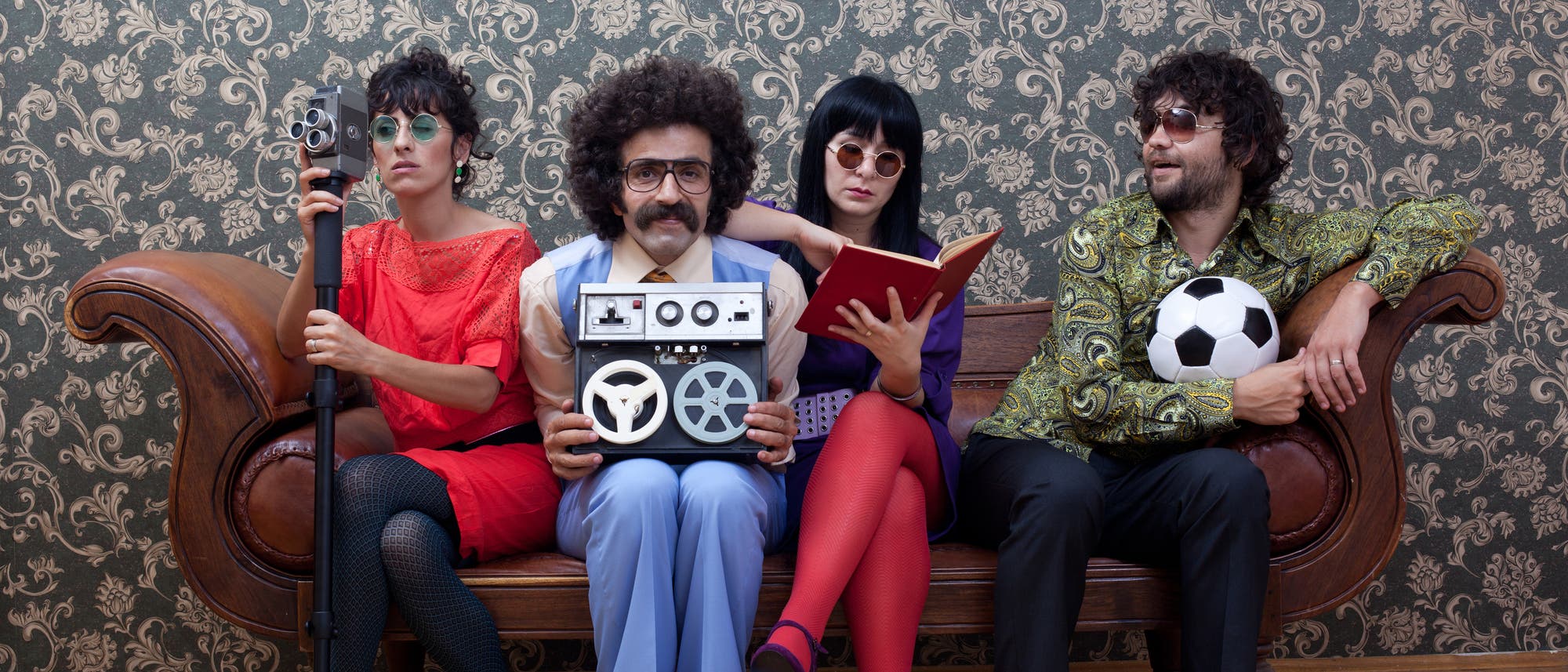 Vier freakige junge Leute im Sixties- oder Seventies-Outfit auf einer Couch