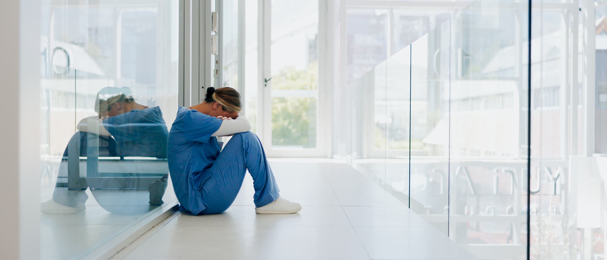 Im Flur eines Krankenhauses sitzt eine Ärztin oder Krankenschwester mit gesenktem Kopf auf dem Boden