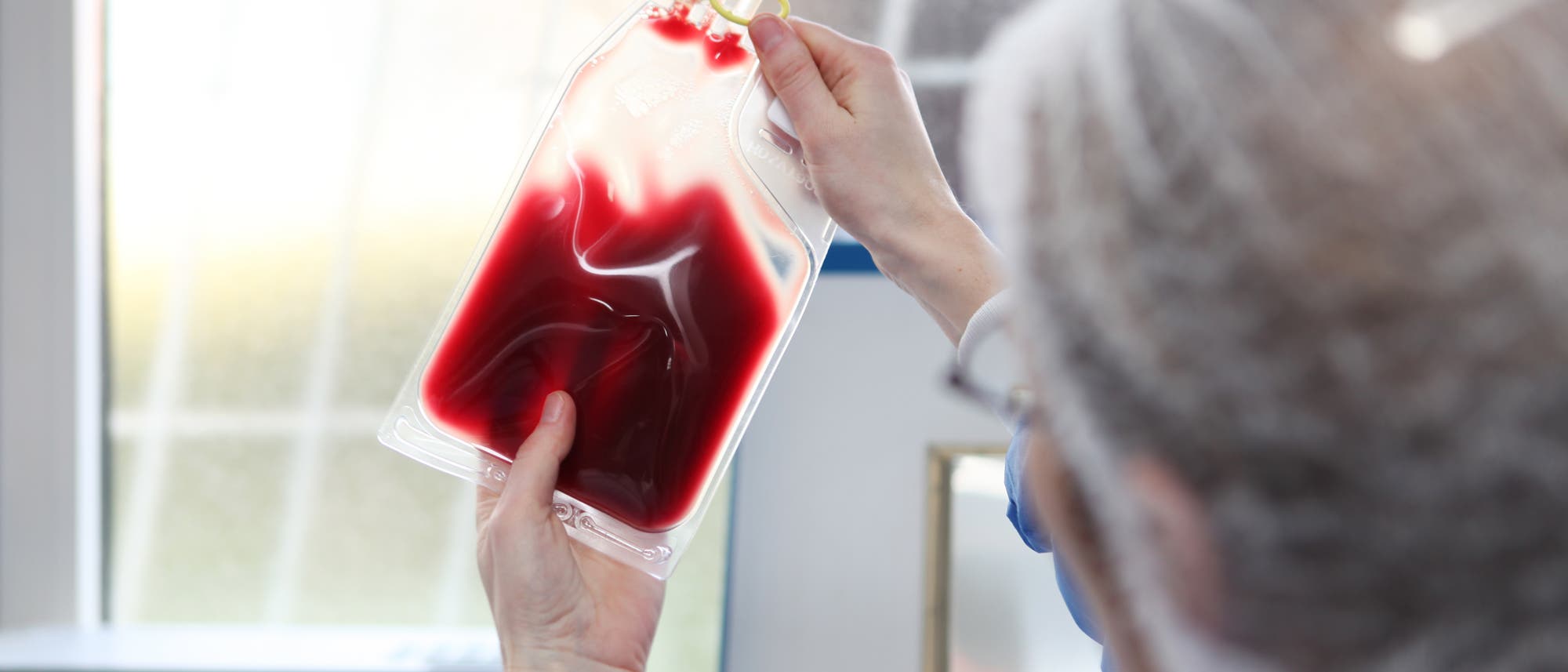 Ein Arzt in Hazmat-Kleidung hält eine Blutkonserve gegens Licht.