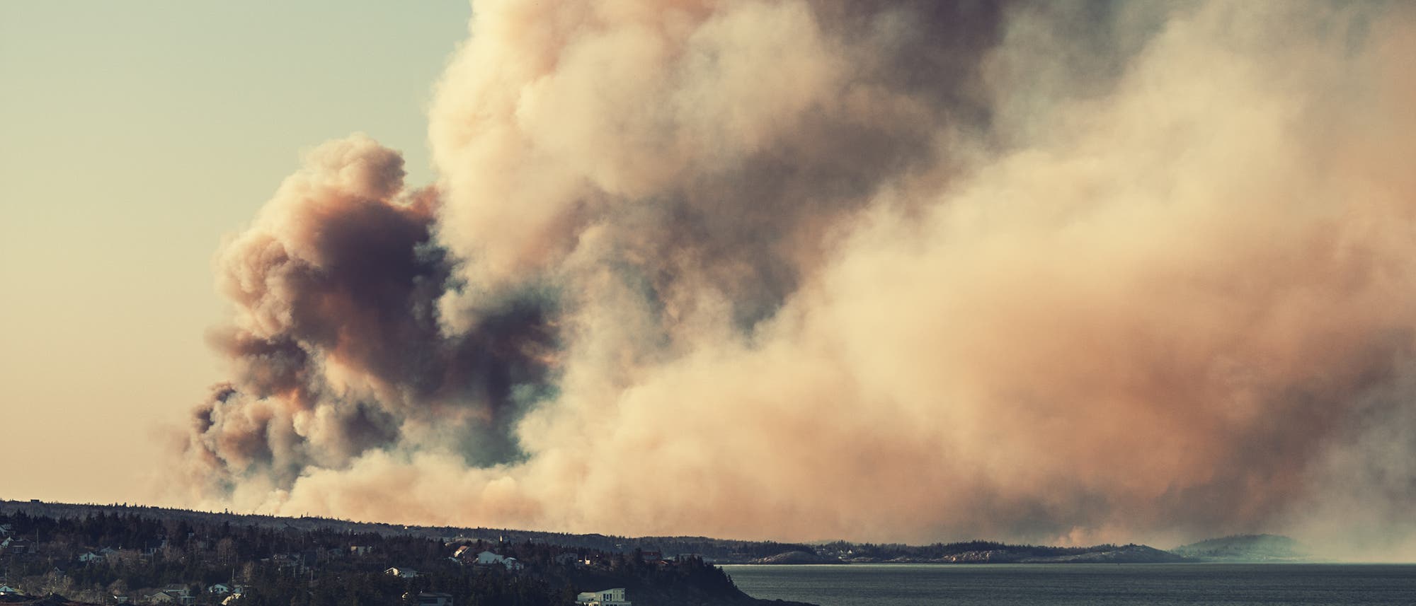 Rauch eines Waldbrandes steigt hoch über die Landschaft.