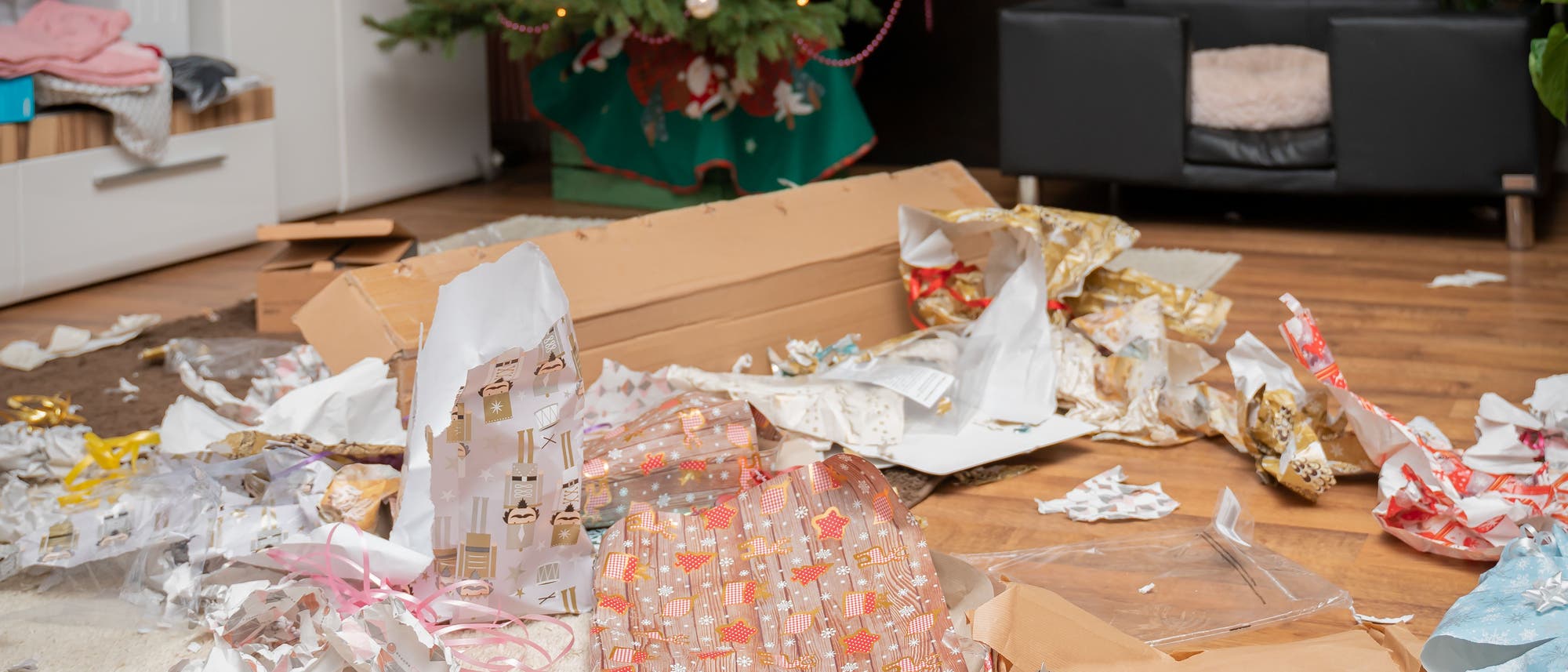 Ein Haufen zerrissenes Geschenkpapier liegt unterm Weihnachtsbaum