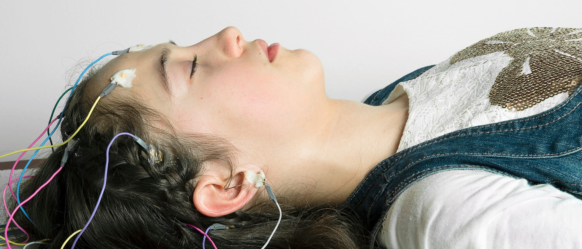 Eine Frau liegt auf dem Boden. An ihrem Kopf sind Elektroden angeschlossen.