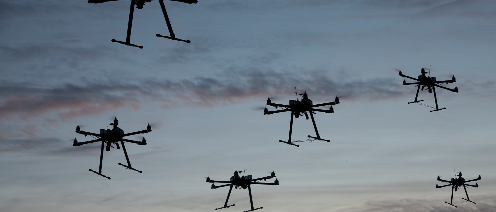 Mehrere Drohnen mit sechs Rotoren im Flug gegen den Himmel fotografiert. 