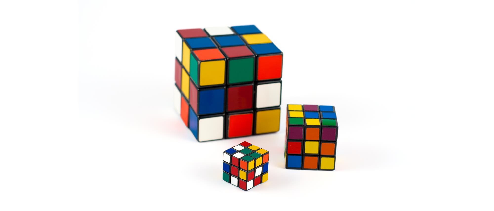 Drei Rubik-Würfel unterschiedlicher Größe auf weißem Grund.
