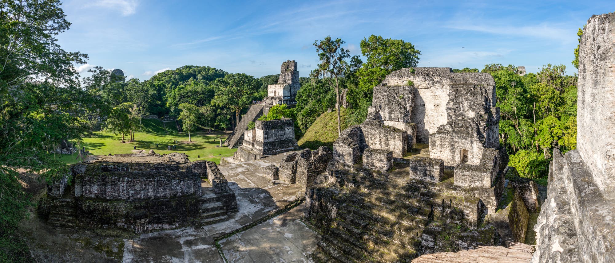 Blick von einer bin in mehrere Meter Höhe erhaltenen Maya-Ruine auf die Rasenfläche davor.