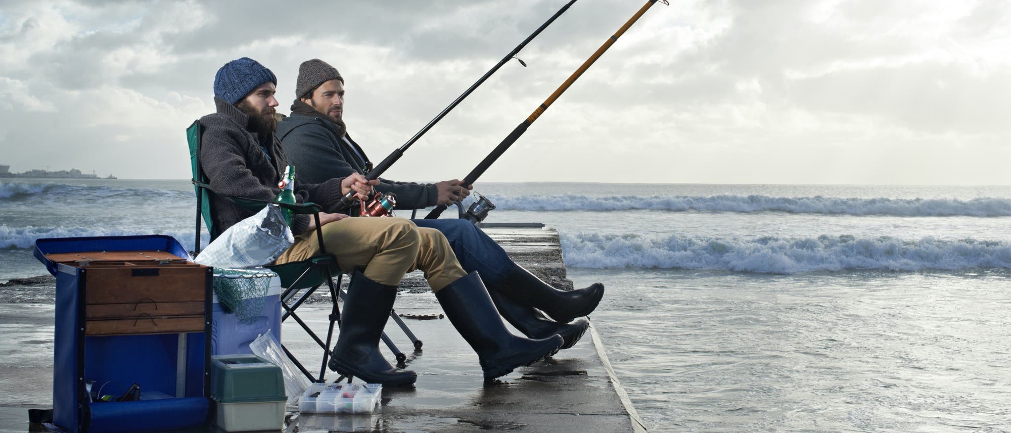 Zwei junge Männer angeln am Meer unter wolkenverhangenem Himmel