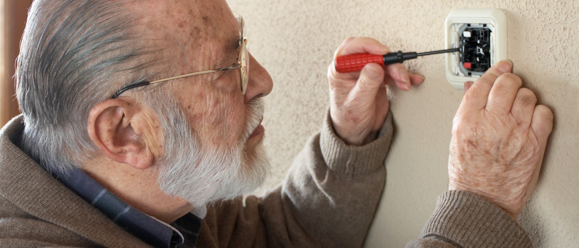 Ein älterer Herr steckt einen Schraubenzieher in eine offene Steckdose