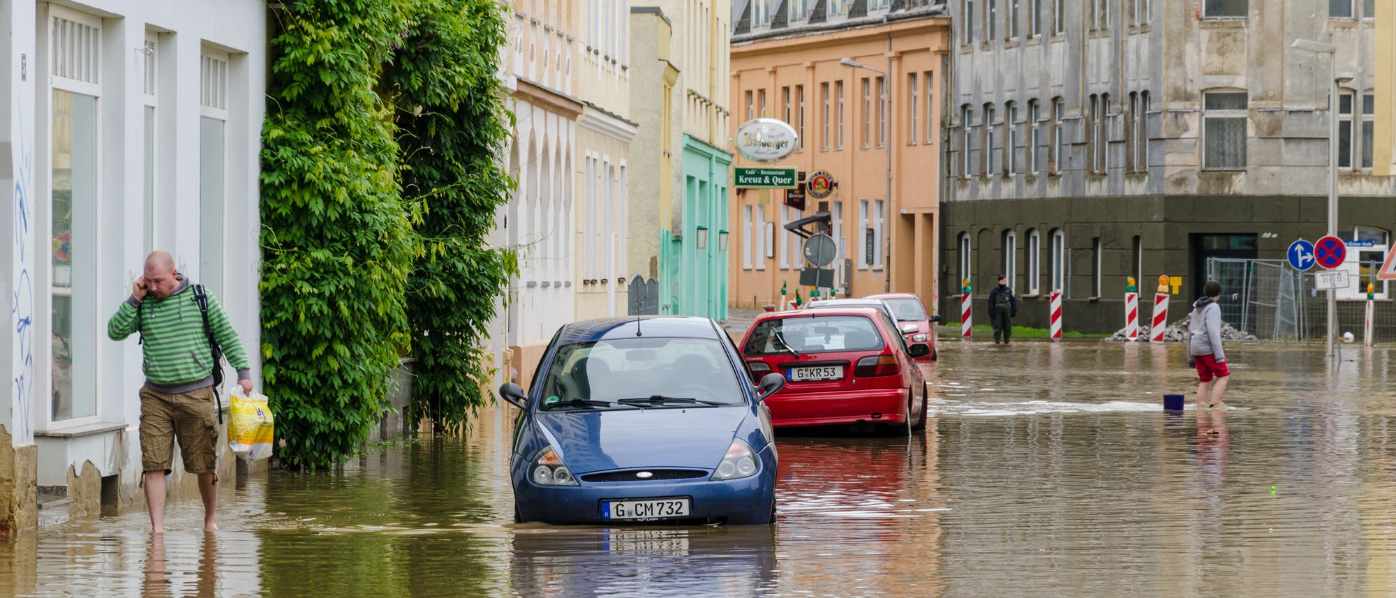 Überschwemmte Straße mit im Wasser stehenden Autos und vermutlich vollgelaufenen Kellern.