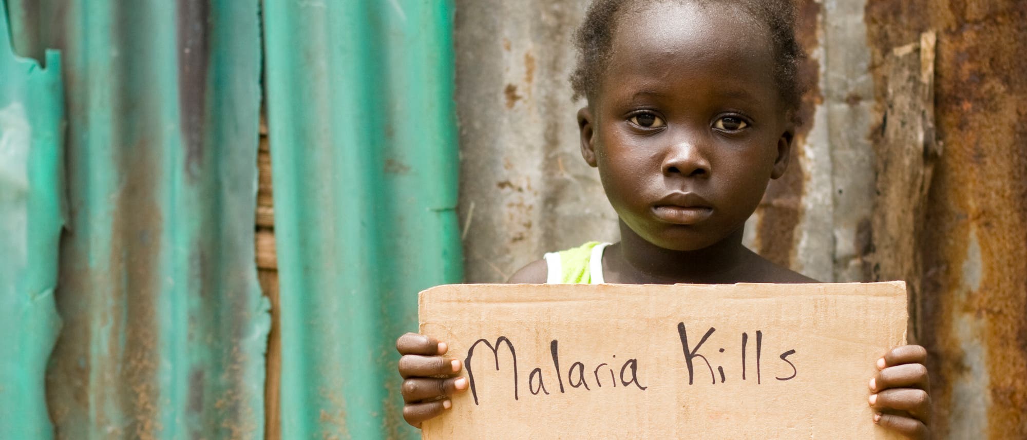 Ein afrikanisches Kind hält ein Schild mit der Aufschrift "Malaria Kills" (Malaria tötet) hoch.