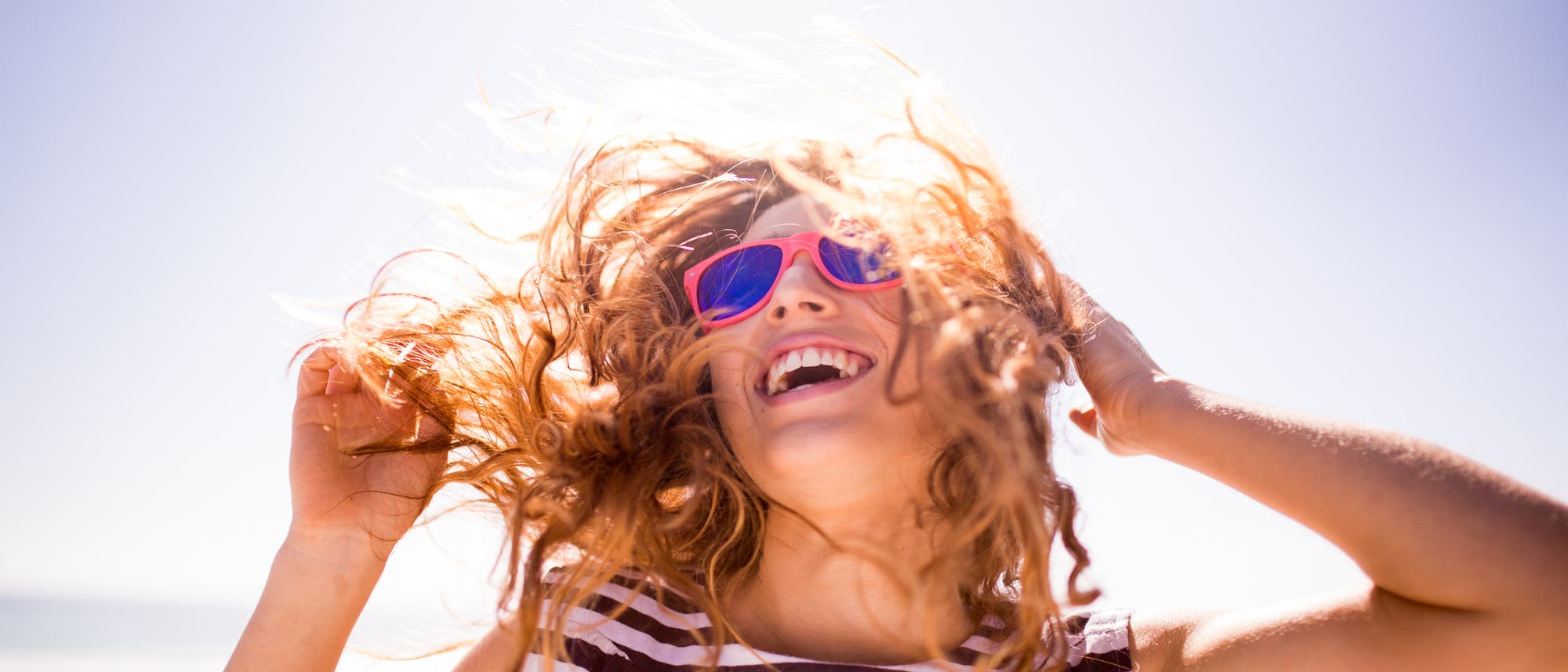 Eine junge Frau mit pinker Sonnenbrille lächelt, weil die Sonne scheint