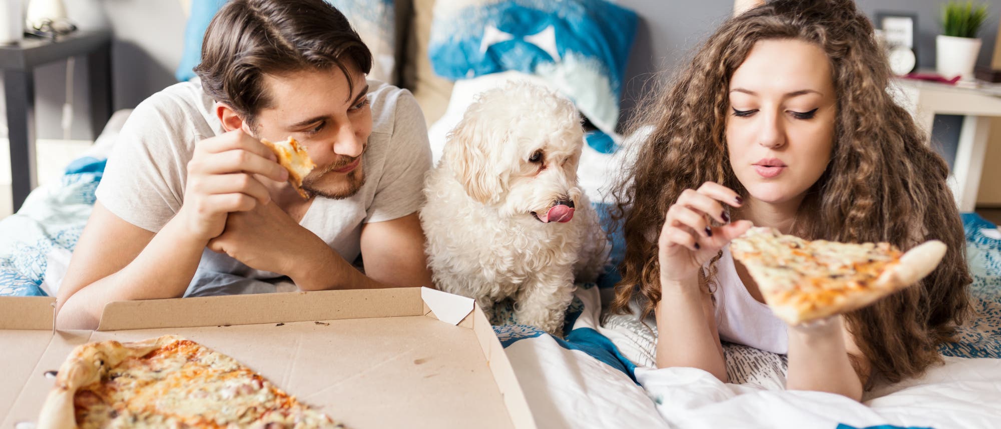 Paar liegt auf dem Bett und isst Pizza. Nein, das ist keine Netflix-Werbung. Nicht mal implizit.