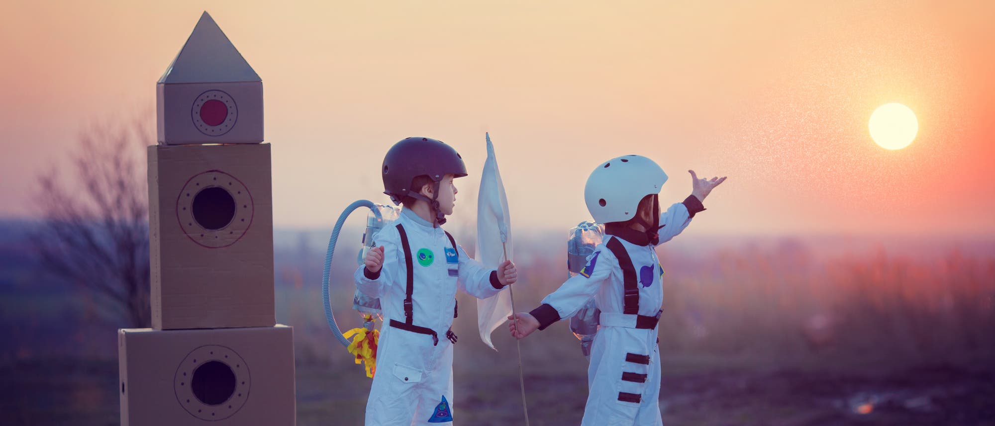 Zwei Kinder im Astronautenkostüm neben einer Rakete