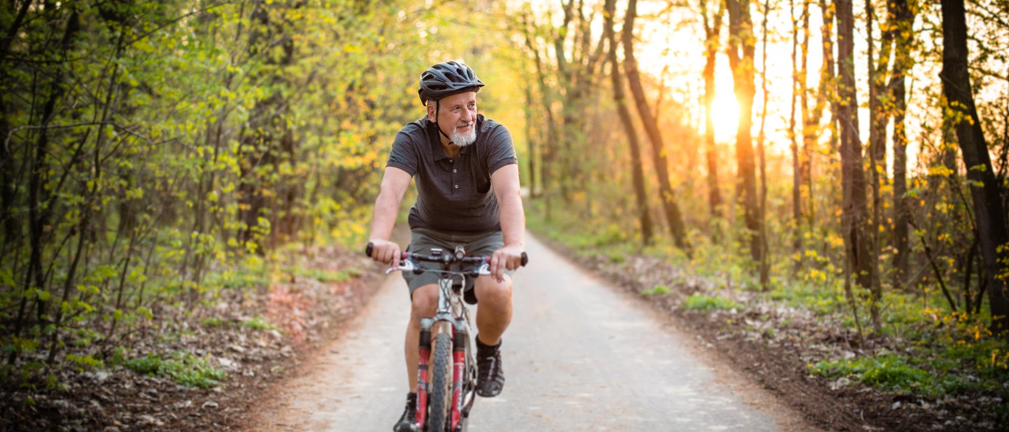 Ein älterer Herr fährt fröhlich und gemütlich mit seinem Rad durch den Wald