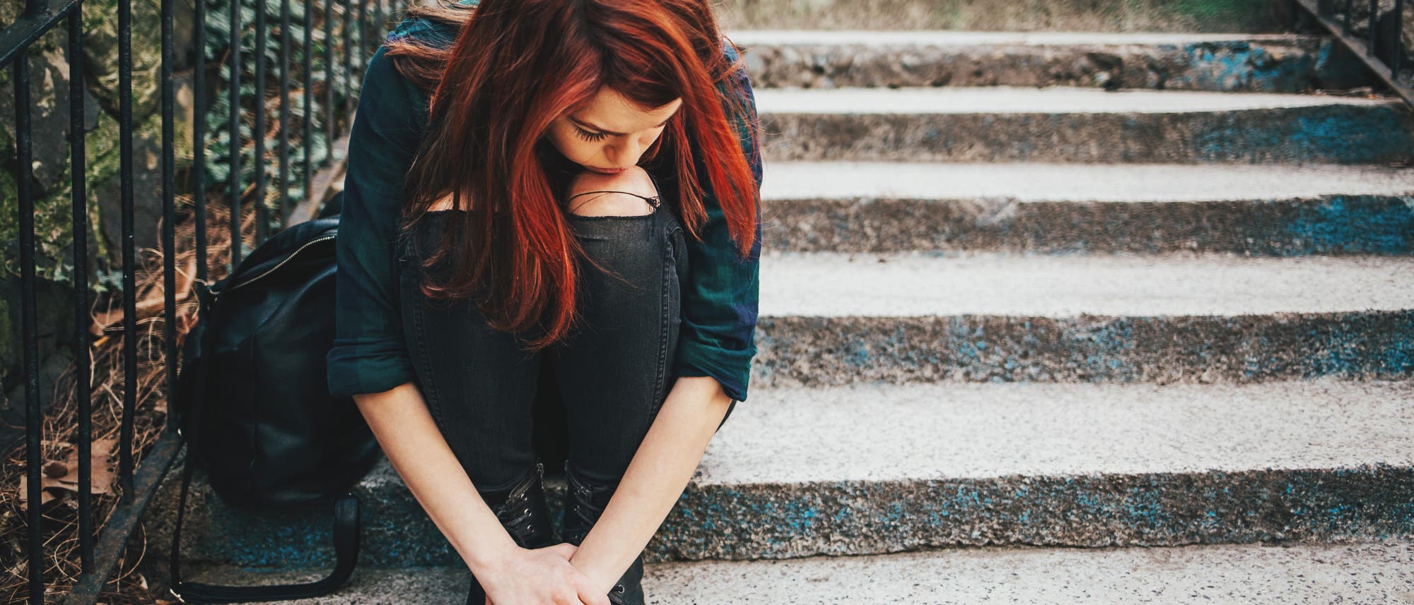 Eine traurige Jugendliche sitzt allein mit gesenktem Kopf auf einer Treppe