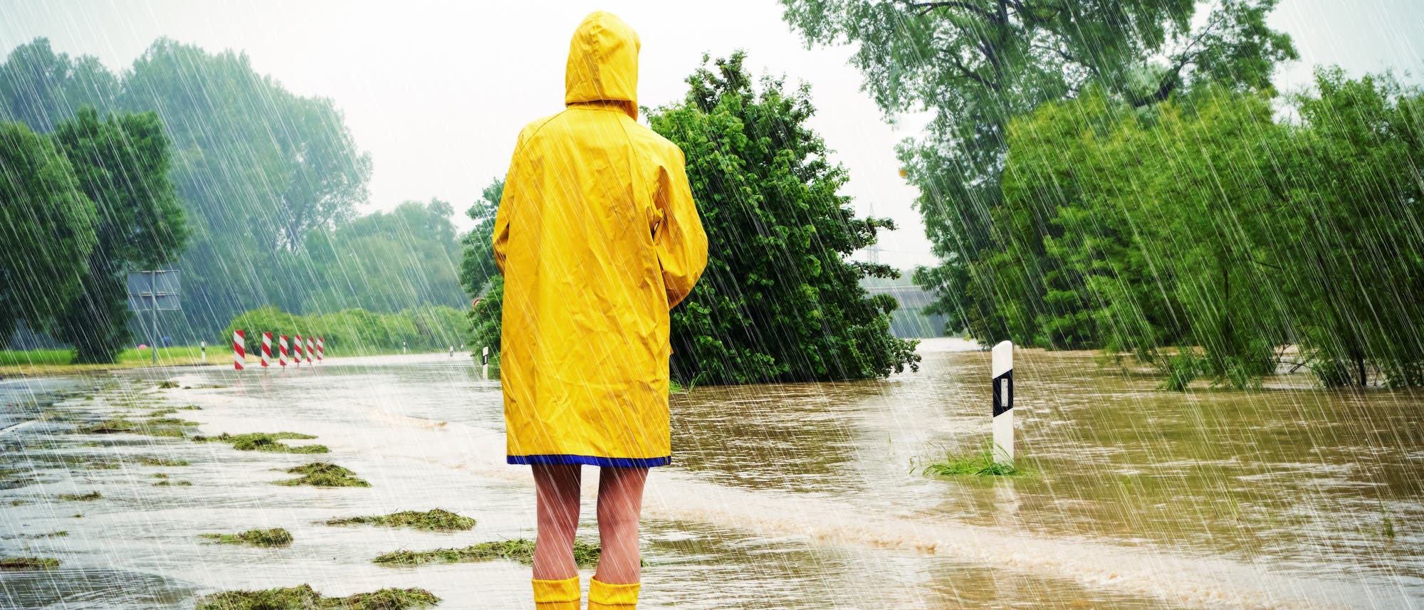 Mädchen im Regenmantel auf überfluteter Straße