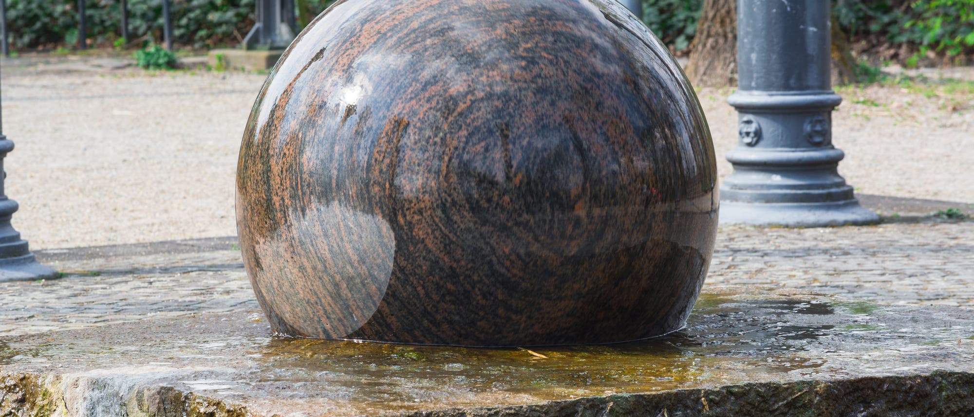 In einem öffentlichen Park dreht sich eine große Kugel aus Granit auf einer passenden Basis, geschmiert von einer dünnen Wasserschicht