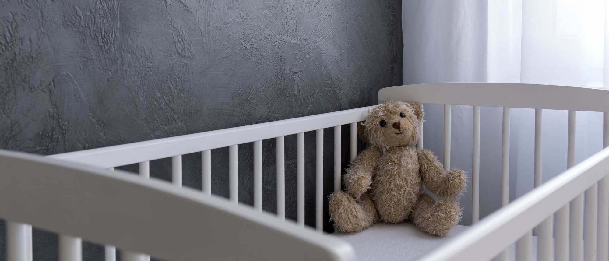 Teddy sitzt in leerem Kinderbett