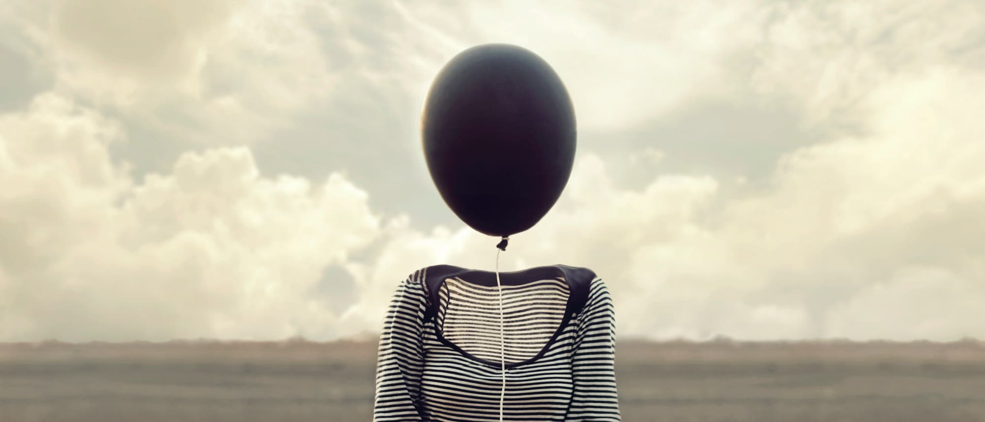 Ein Frau ohne Kopf hält einen schwarzen Luftballon in der Hand.