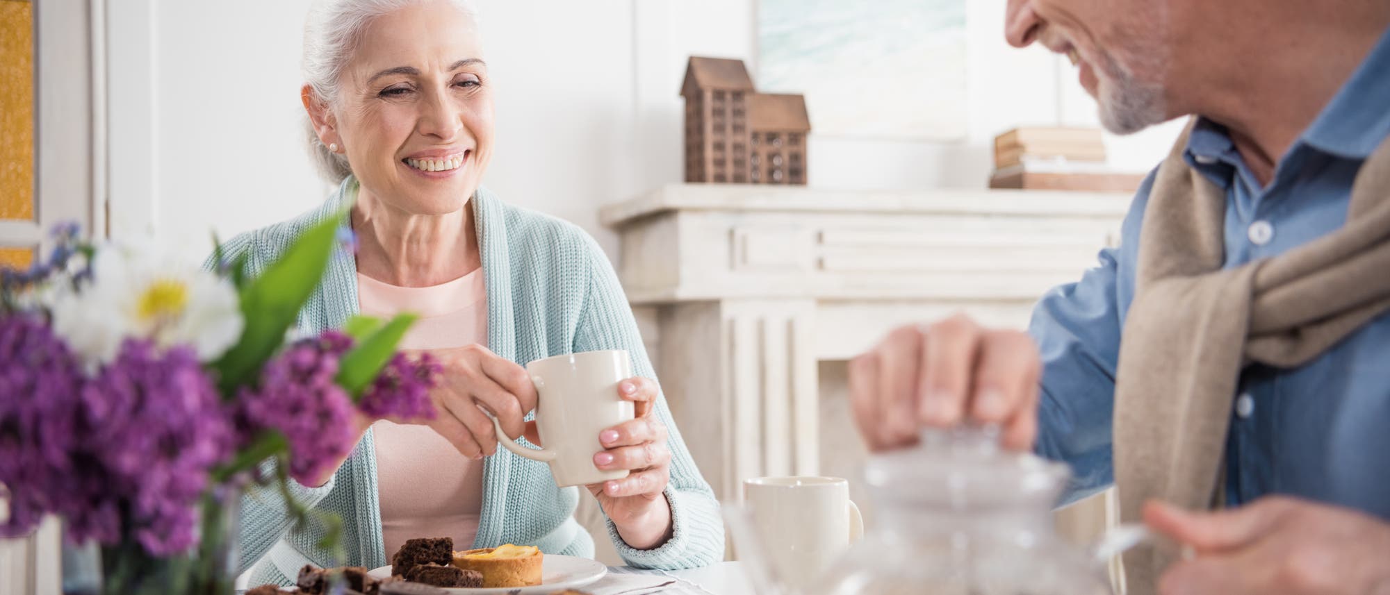 Eine ältere Frau und ein älterer Mann sitzen zusammen an einem Tisch und trinken Tee und essen Plätzchen.