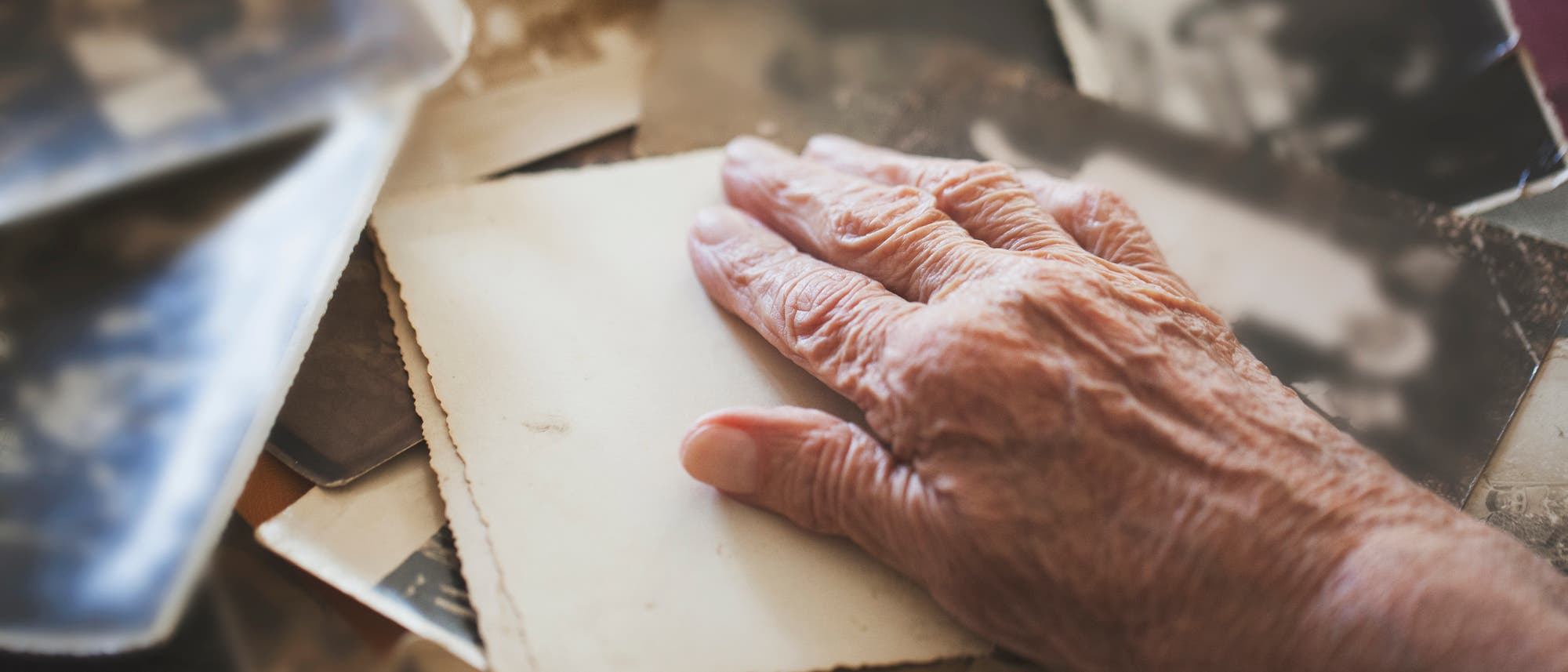 Hand von alter Person liegt auf schwarz-weiß Fotos
