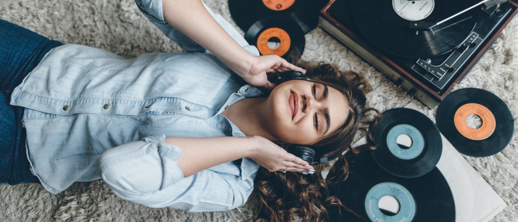 Frau hört Musik über Kopfhörer inmitten ihrer Schallplatten