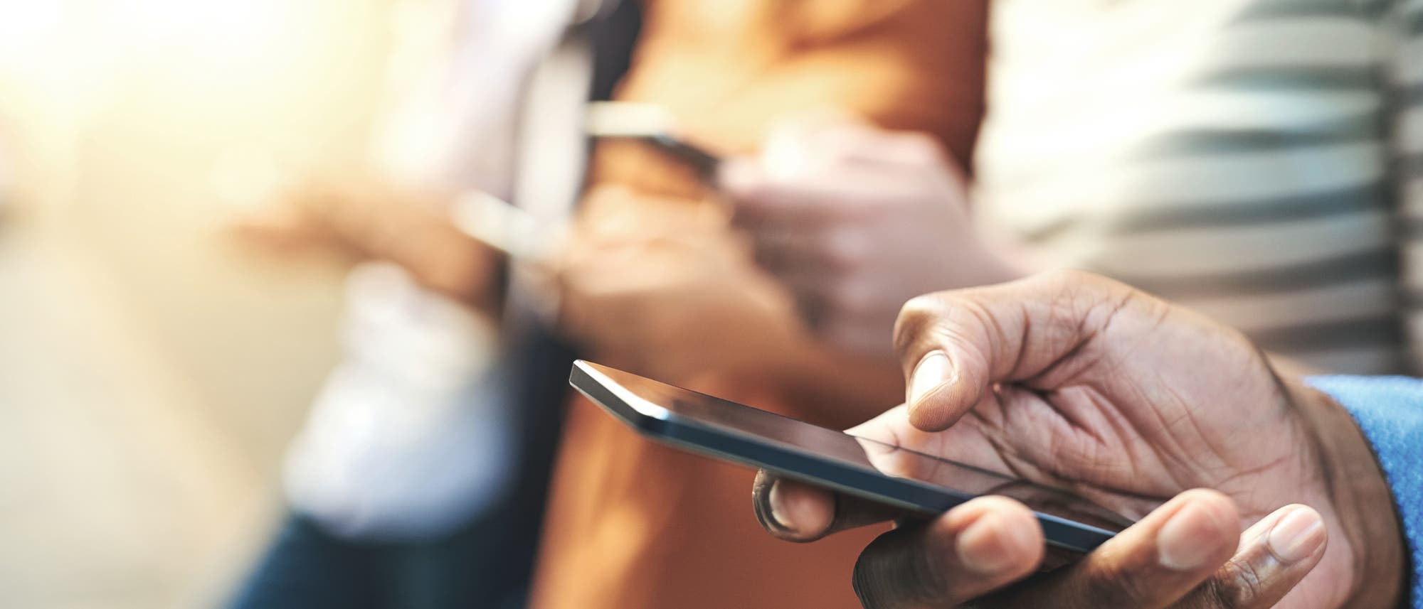 Mehrere Hände, die Smartphones halten und bedienen, die vordere in scharf, die hinteren Personen in Unschärfe.