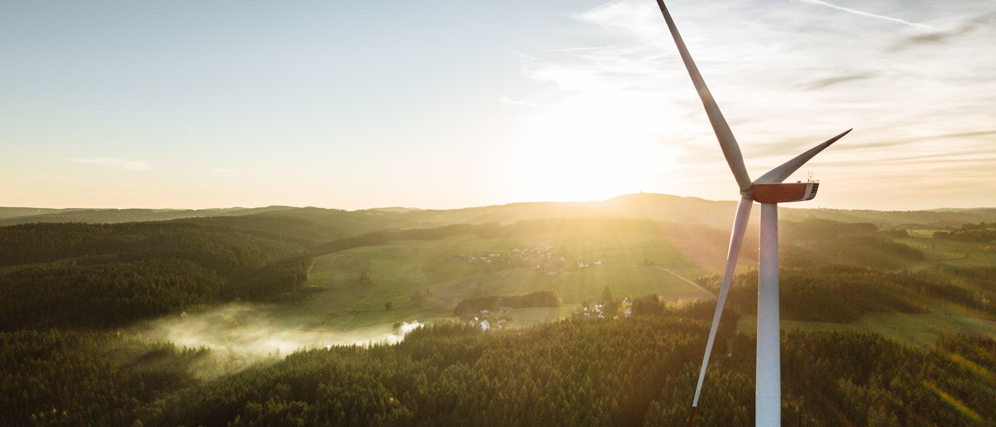Die Turbine eines Windrads, das auf einem Feld steht. Im Hintergrund ein Sonnenuntergang.